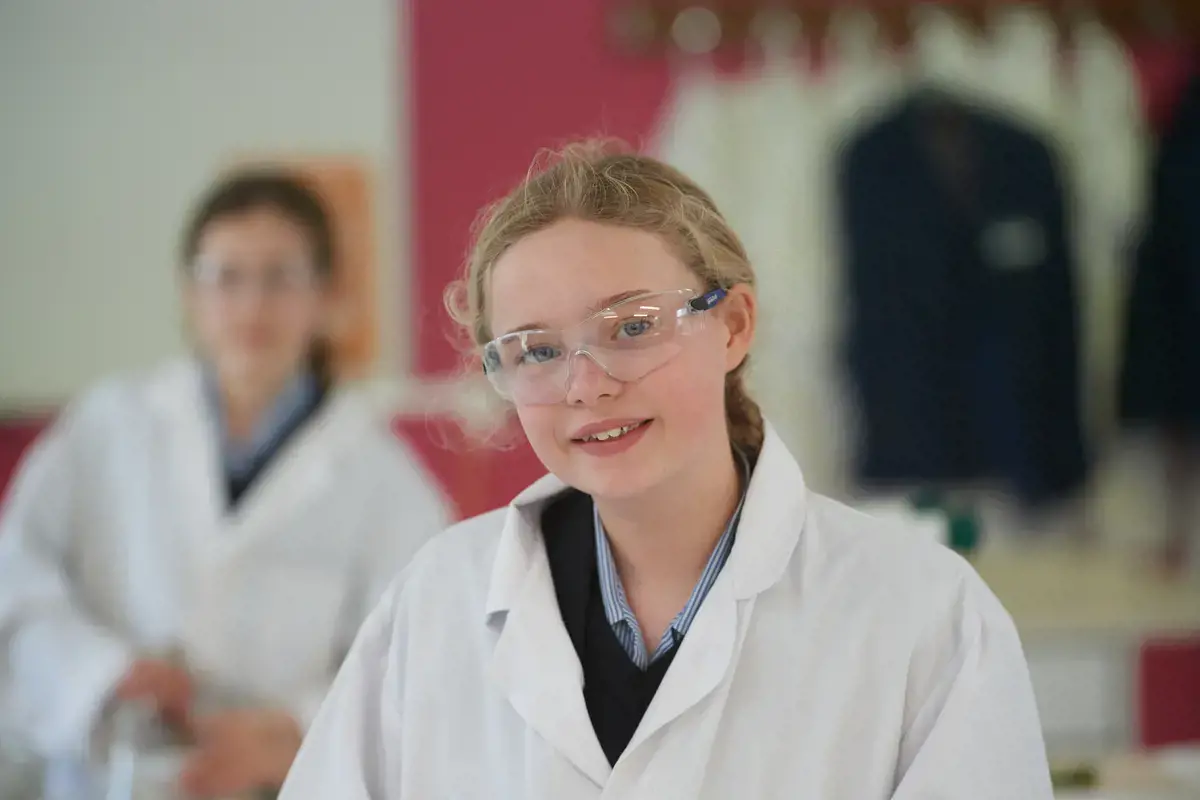 Girl in science class, wearing a lab coat and protective goggles