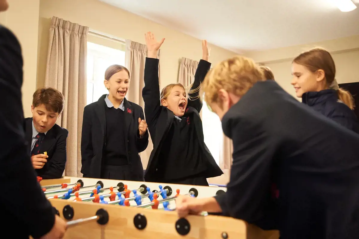 A group of pupils playing table football, one girl is celebrating a goal!