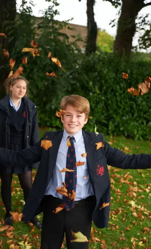 A happy student playing with leaves in the school grounds
