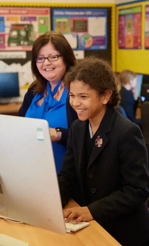 A happy student working on a computer with support from her teacher